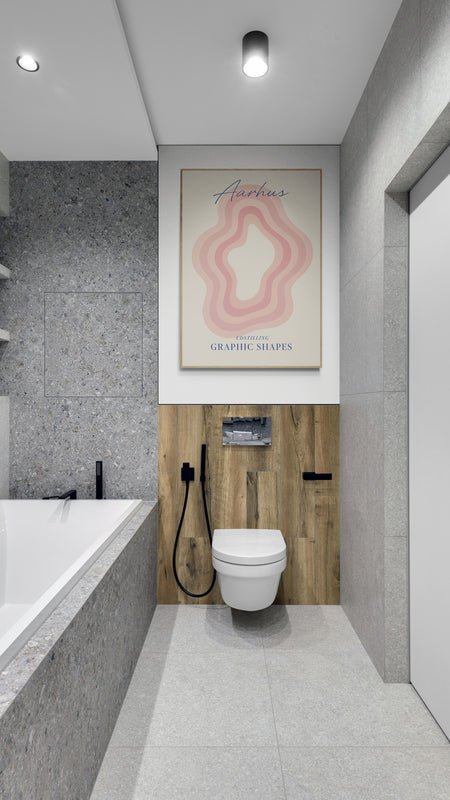 Plakat z napisem "Aarhus" i różowym graficznym wzorem zawieszony nad toaletą w nowoczesnej łazience z drewnianym panelem i szarymi płytkami