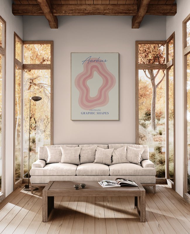Plakat z napisem "Aarhus" i abstrakcyjnym wzorem w odcieniach różu zawieszony nad beżową sofą w przytulnym salonie z drewnianym sufitem i dużymi oknami
