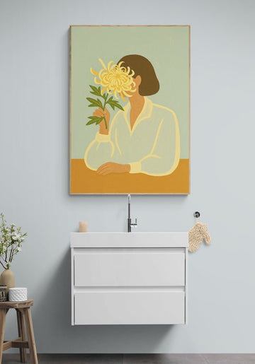 Plakat z ilustracją kobiety trzymającej chryzantemę, zawieszony nad białą umywalką w minimalistycznej łazience o jasnych ścianach