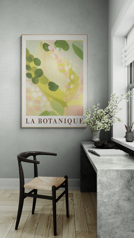 Plakat z napisem "La Botanique" i pastelowym motywem roślinnym, zawieszony nad betonowym biurkiem przy oknie z kwiatami i czarnym krzesłem