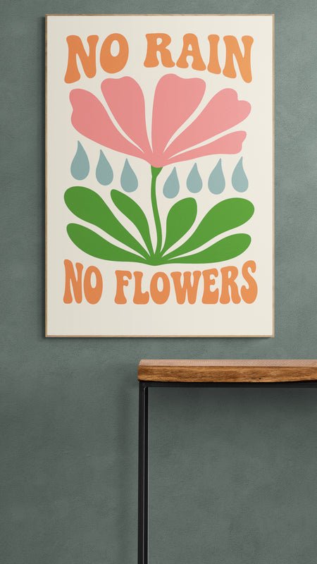 Plakat z napisem "No Rain No Flowers" i kolorową grafiką kwiatu zawieszony na zielonej ścianie nad minimalistyczną konsolą z drewnianym blatem