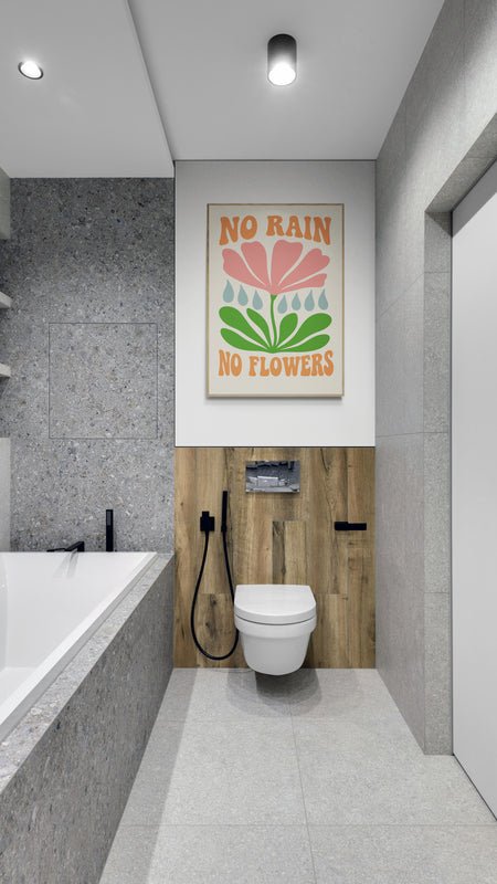 Plakat z napisem "No Rain No Flowers" i kolorową grafiką kwiatu zawieszony nad toaletą w nowoczesnej łazience z drewnianym akcentem i szarymi płytkami
