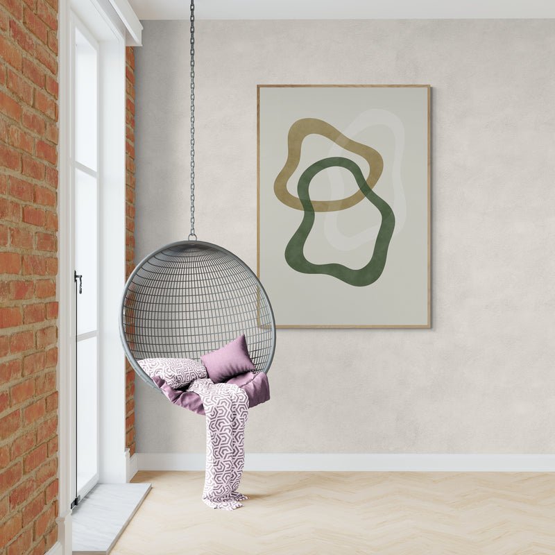 Minimalistyczny plakat z organicznymi kształtami w zieleni i oliwce na jasnym tle, zawieszony w przytulnym kąciku z wiszącym fotelem z poduszkami i kocem w odcieniach fioletu.