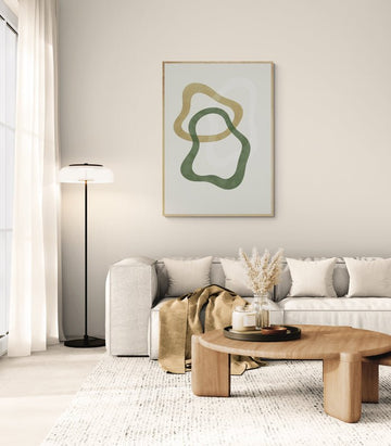 Minimalistyczny plakat z organicznymi kształtami w zieleni i oliwce na jasnym tle, zawieszony nad sofą w przytulnym salonie urządzonym w stylu skandynawskim z jasnymi tkaninami i drewnianym stolikiem.